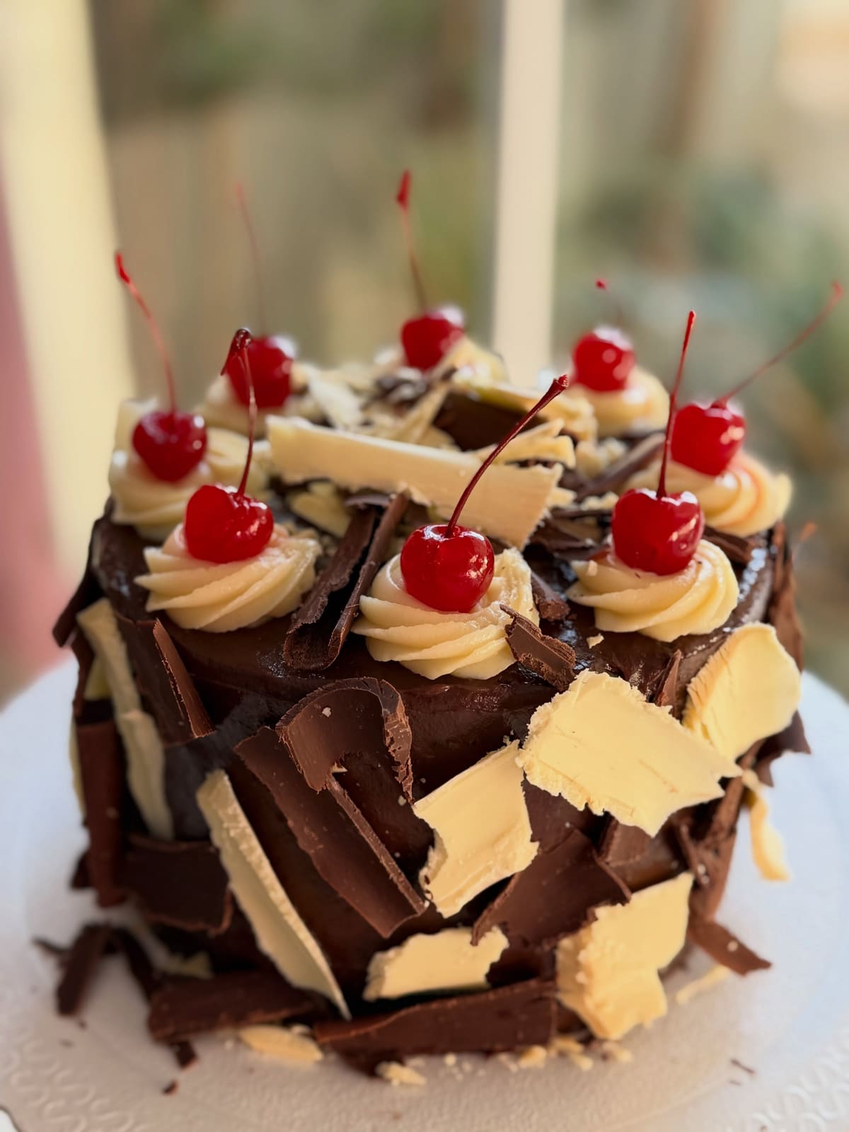 Bolo coberto com lascas de chocolate ao leite e branco, chantilly e cerejas
