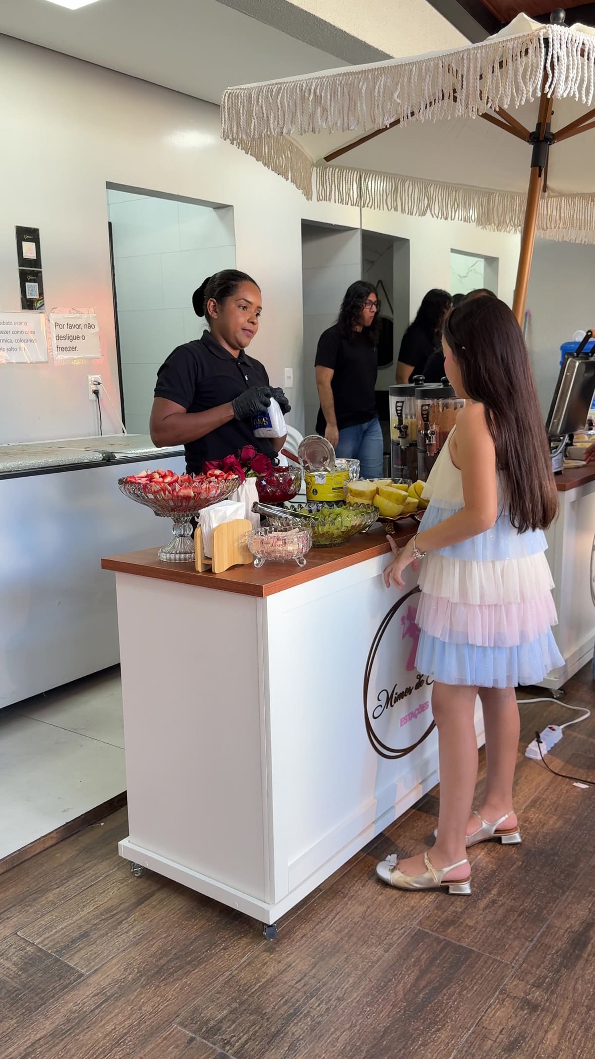 Atendente servindo frutas na estação, com convidados diante do balcão